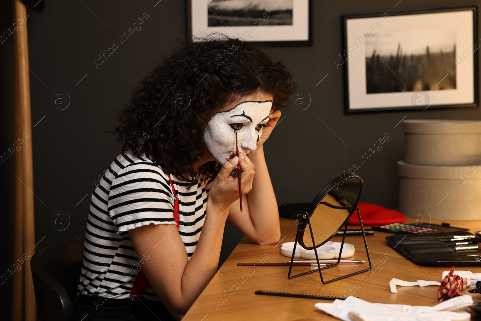 Photo of Young woman applying mime makeup near mirror indoors