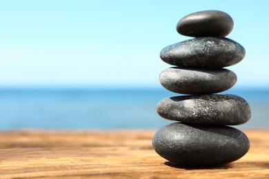 Photo of Stack of stones on wooden table against seascape, space for text. Zen concept