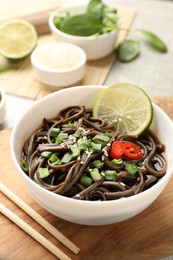 Photo of Tasty buckwheat noodles (soba) with sauce, onion and lime in bowl on table