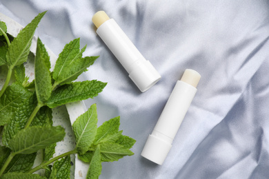 Photo of Hygienic lipsticks and mint leaves on light silk fabric, flat lay