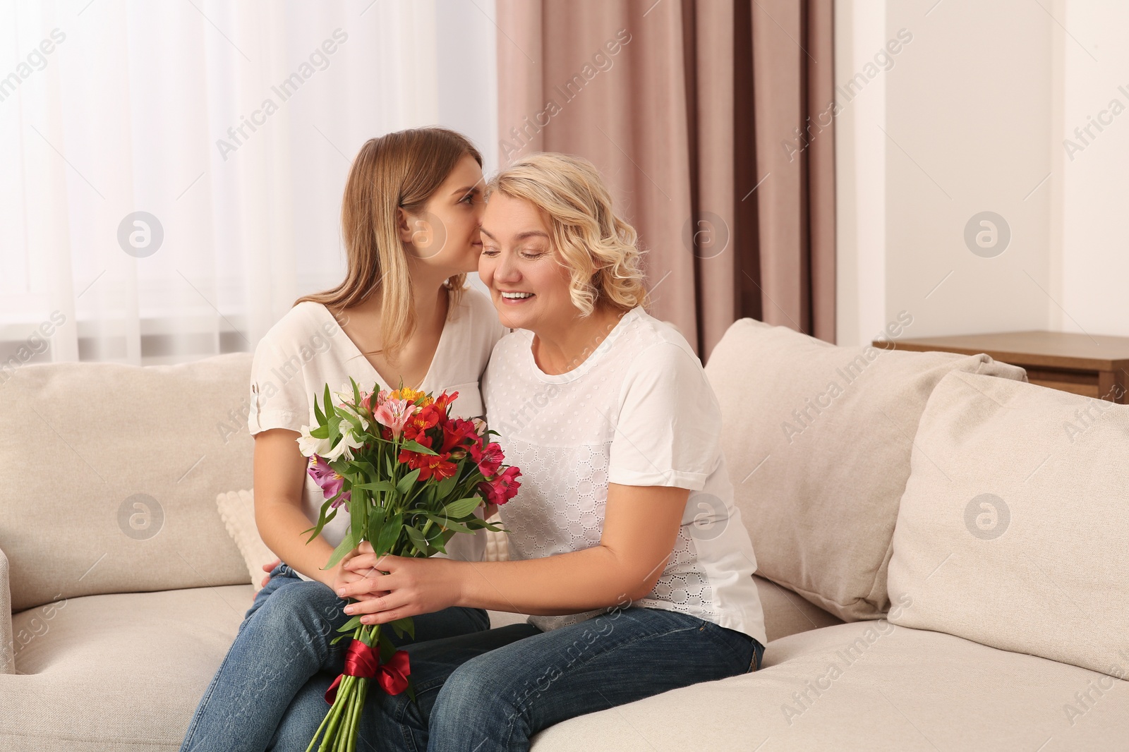 Photo of Young daughter congratulating her mom with flowers at home. Happy Mother's Day