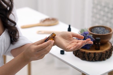 Photo of Woman with bottle applying essential oil onto wrist indoors, closeup