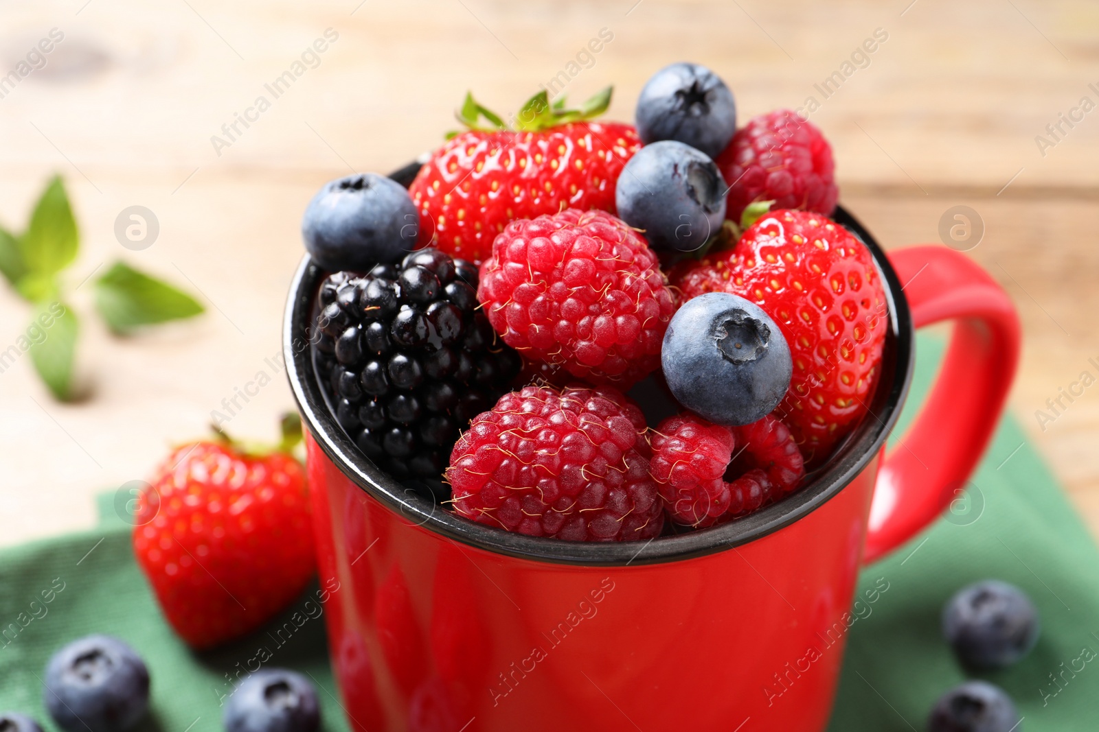 Photo of Many different fresh ripe berries in mug on wooden table, closeup