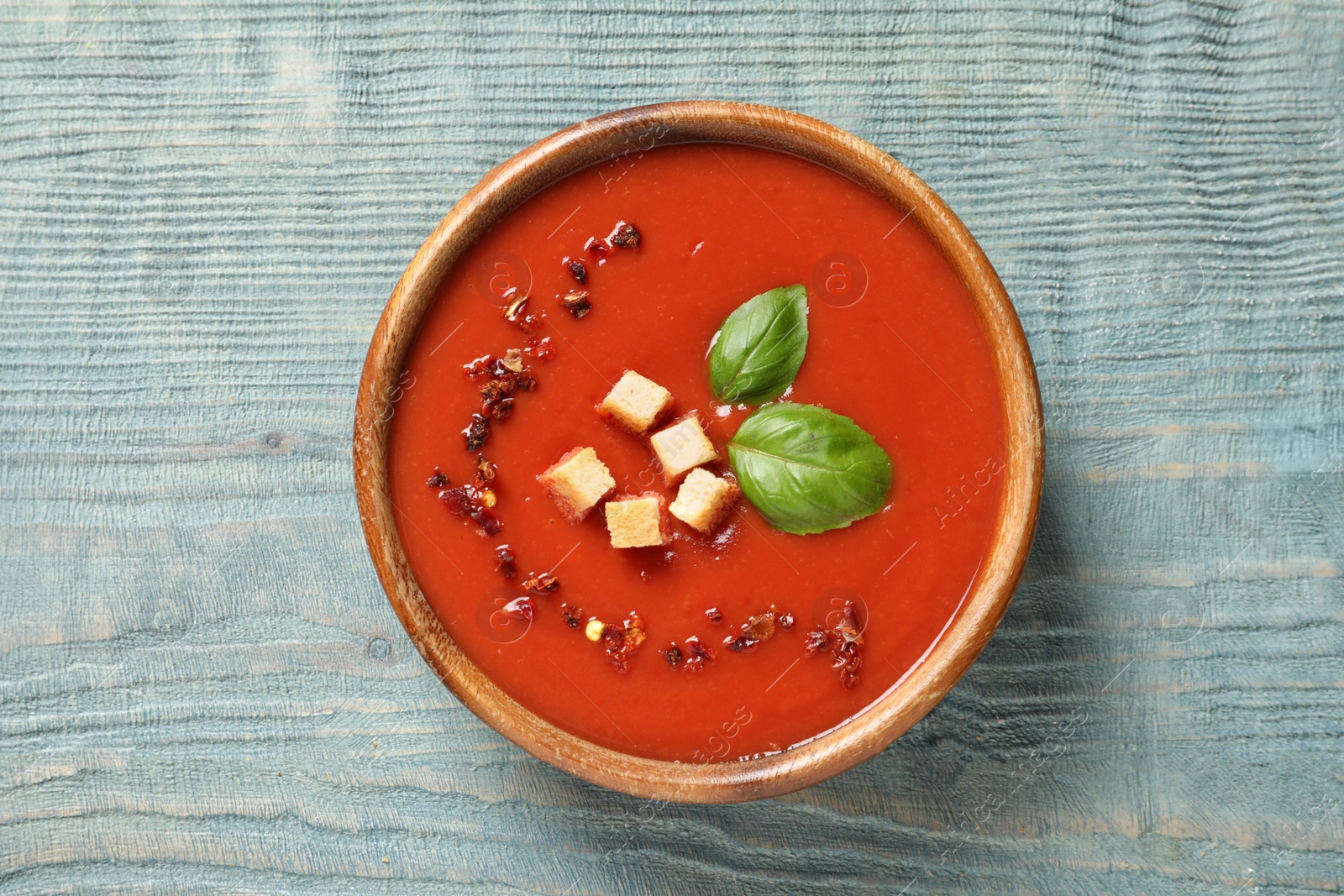 Photo of Bowl with fresh homemade tomato soup on wooden background, top view