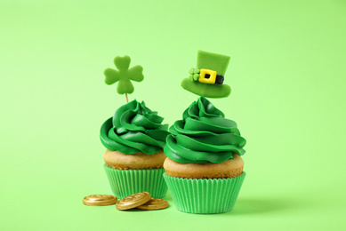 Delicious decorated cupcakes and coins on light green background. St. Patrick's Day celebration