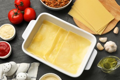 Photo of Cooking lasagna. Pasta sheets in baking tray and products on dark textured table, flat lay