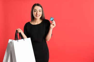 Young woman with credit card and shopping bags on crimson background, space for text. Spending money