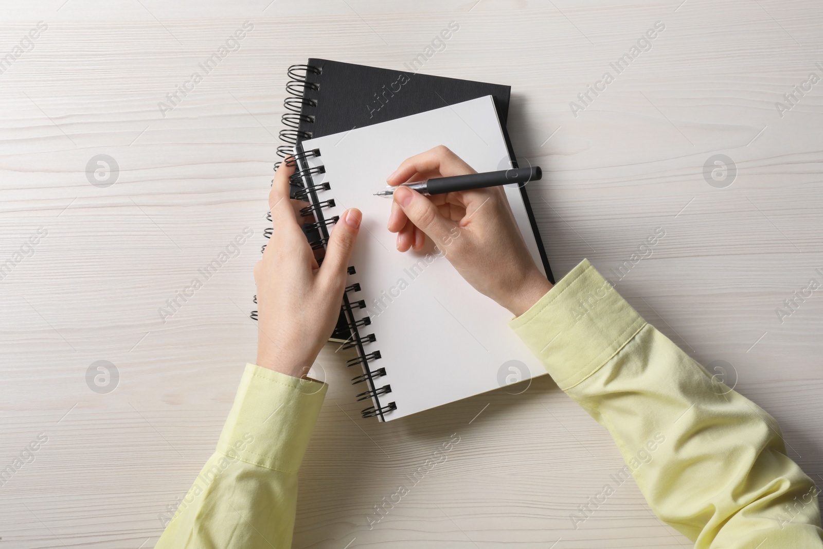 Photo of Woman writing in notebook at white wooden table, top view