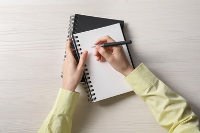 Woman writing in notebook at white wooden table, top view