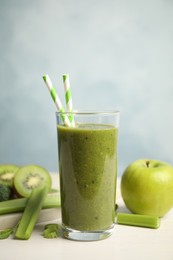 Photo of Delicious green juice and fresh ingredients on white table against light blue background