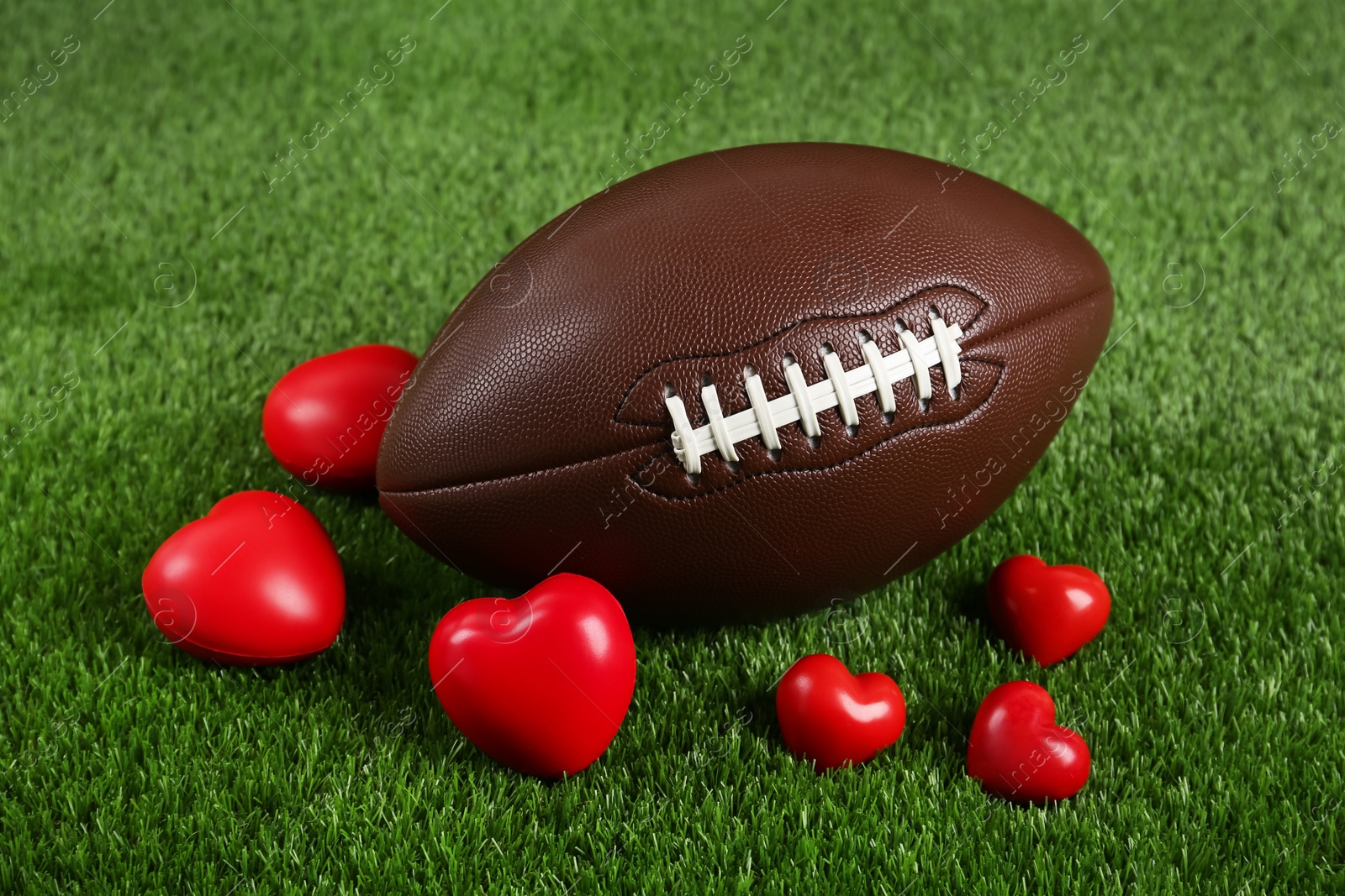 Photo of American football ball and hearts on green grass