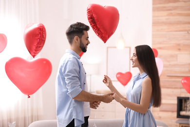 Happy young couple in living room decorated with heart shaped balloons. Valentine's day celebration