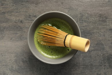 Photo of Cup of fresh matcha tea with bamboo whisk on dark grey table, top view