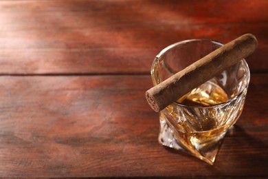 Photo of Glass of whiskey and cigar on wooden table, above view. Space for text