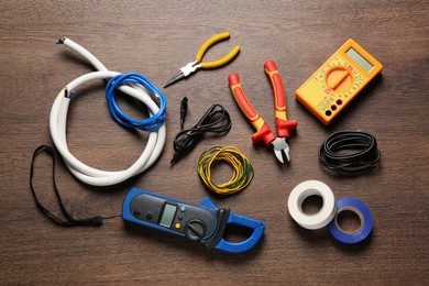 Photo of Different wires and electrician's tools on wooden table, flat lay