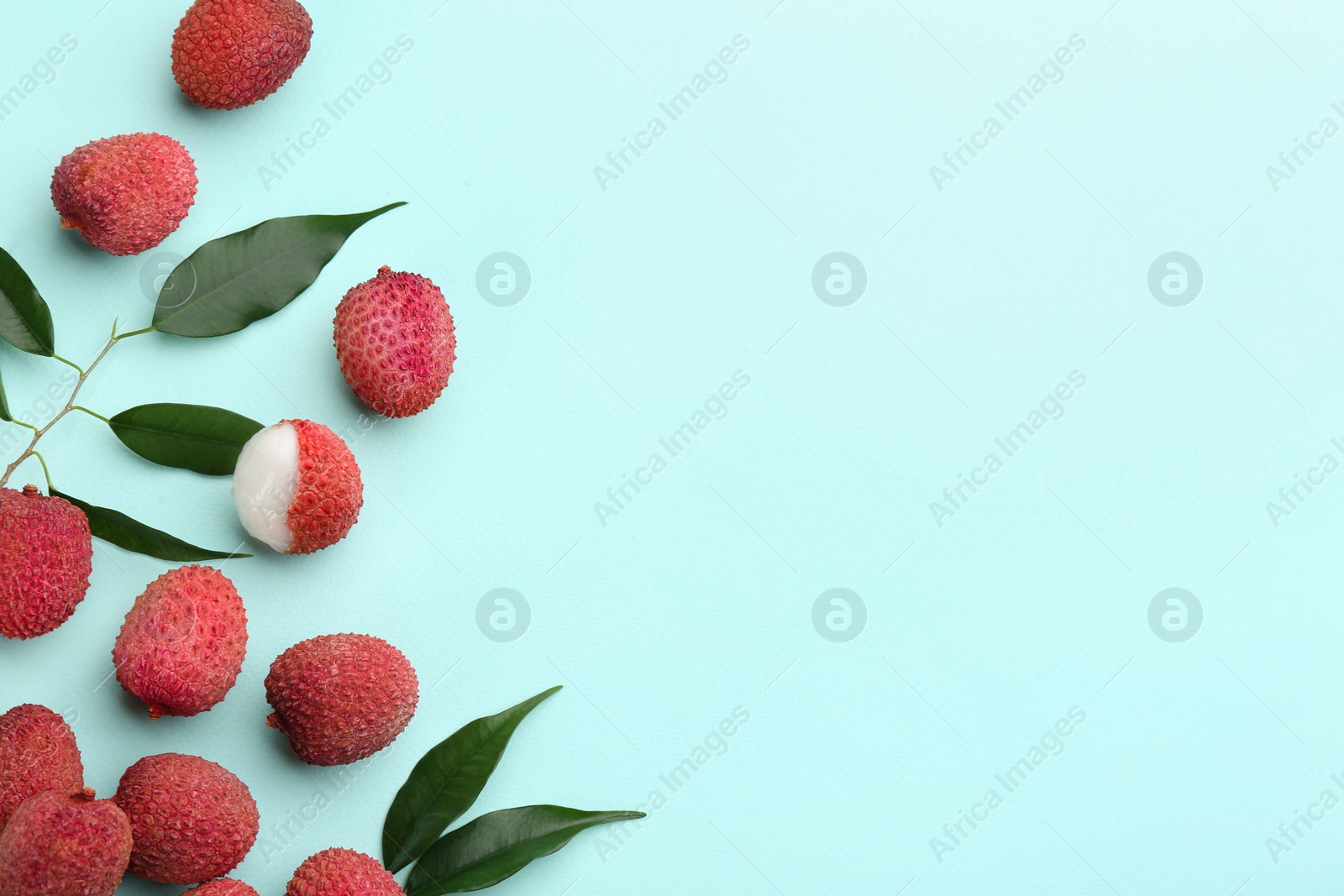 Photo of Fresh ripe lychees with leaves on turquoise background, flat lay. Space for text