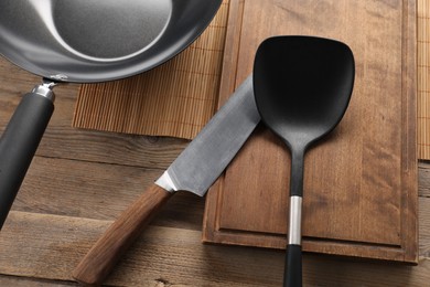 Photo of Black metal wok, knife and spatula on wooden table, above view