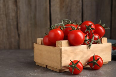 Many ripe red tomatoes in wooden crate on grey table. Space for text