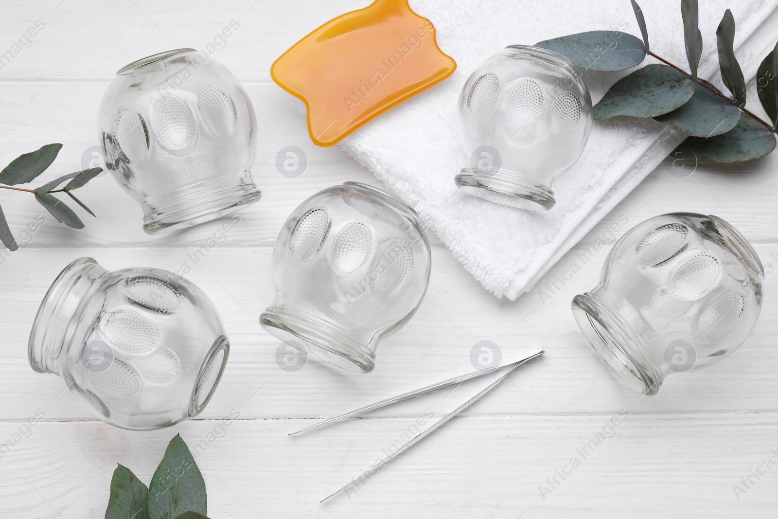 Photo of Cupping set, gua sha and eucalyptus branches on white wooden table, flat lay