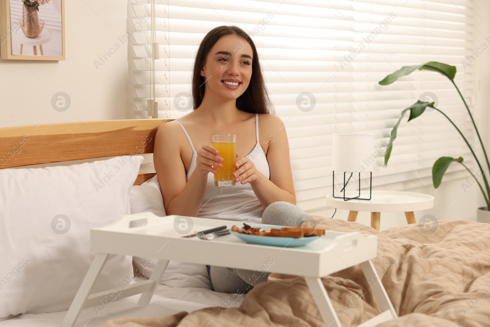 Photo of Happy young woman having breakfast on bed at home