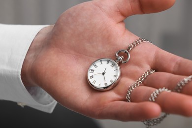 Man holding chain with elegant pocket watch on blurred background, closeup