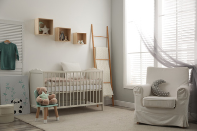 Stylish baby room interior with crib and armchair