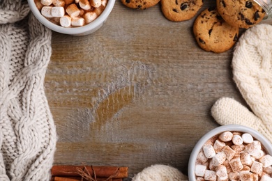 Photo of Frame made with cocoa drink, cookies and warm clothes on wooden table, flat lay. Space for text