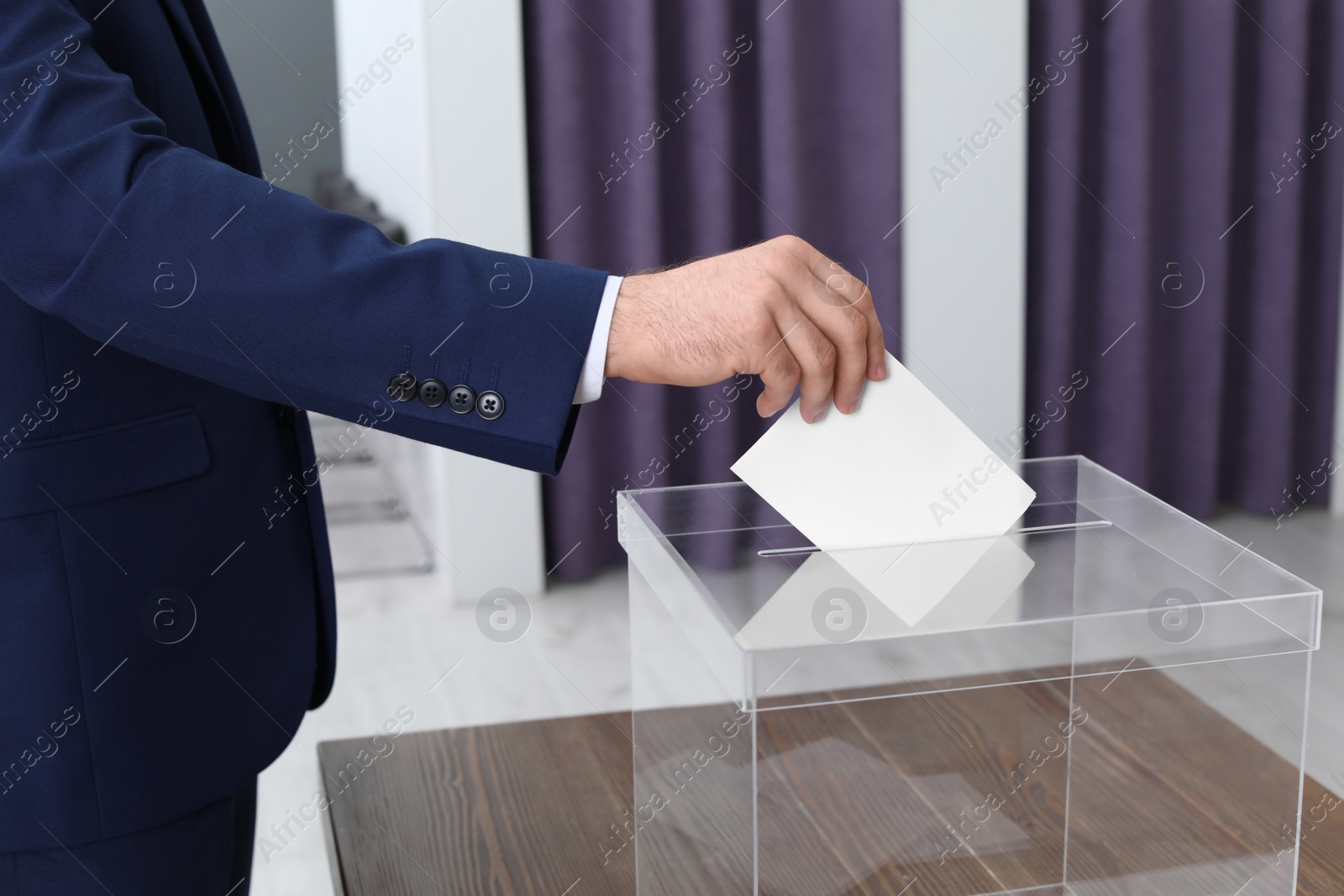 Photo of Man putting his vote into ballot box at polling station, closeup