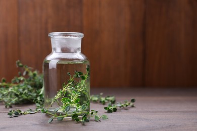 Photo of Thyme essential oil on wooden table, space for text