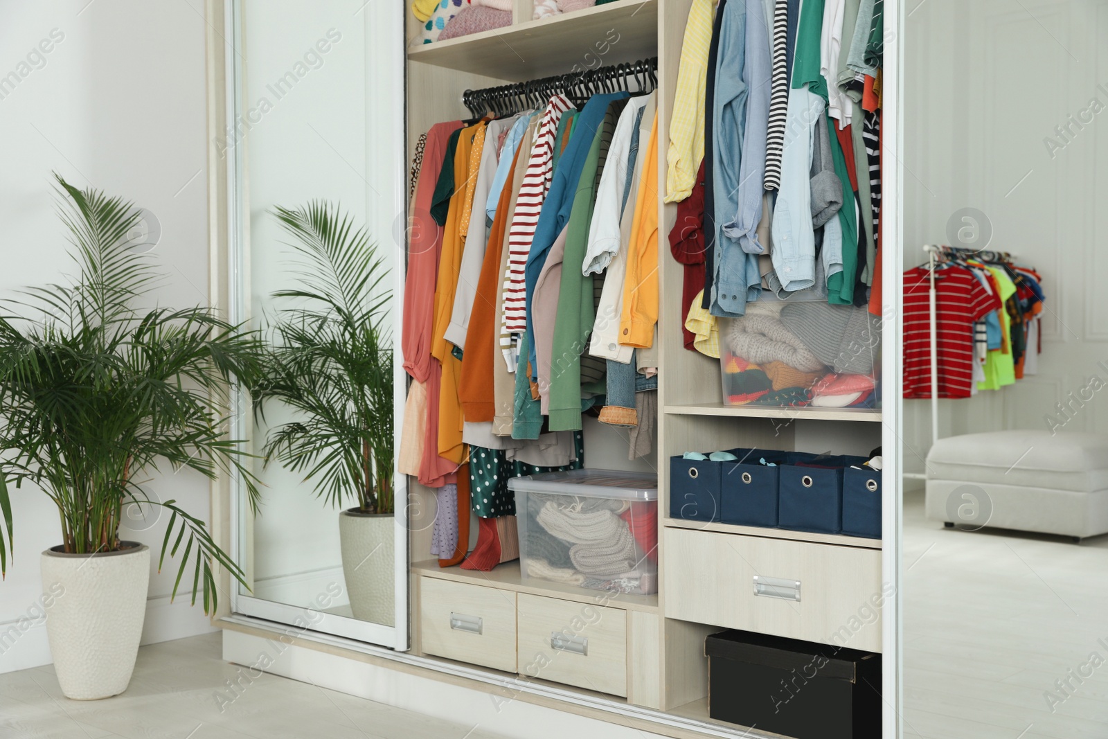 Photo of Wardrobe closet with different stylish clothes and home stuff in room. Fast fashion