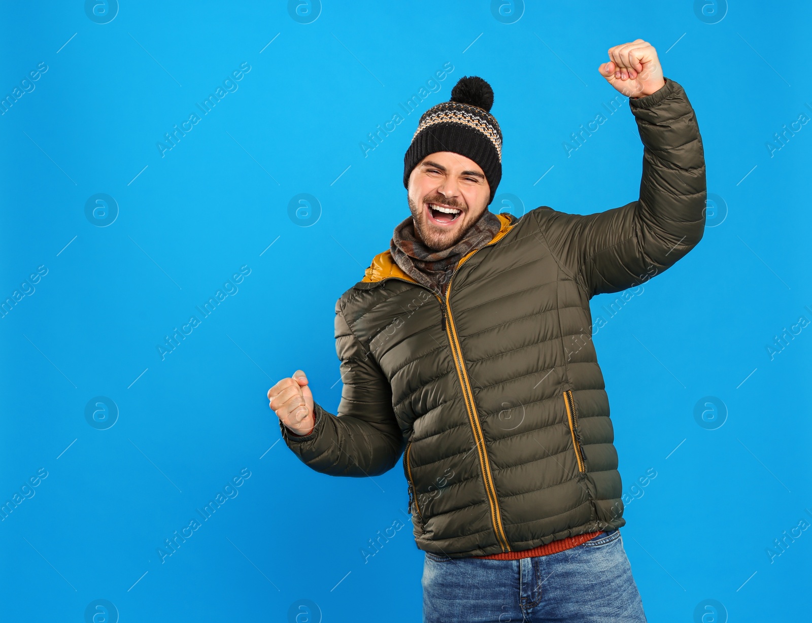 Photo of Happy young man in warm clothes on blue background. Winter vacation