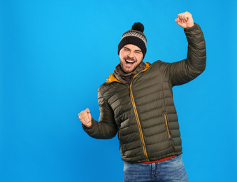 Photo of Happy young man in warm clothes on blue background. Winter vacation