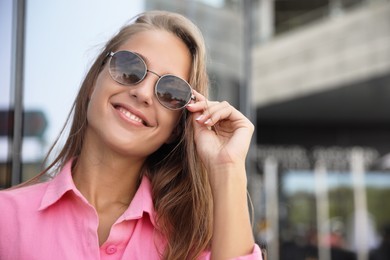 Photo of Beautiful young woman in stylish sunglasses on city street. Space for text