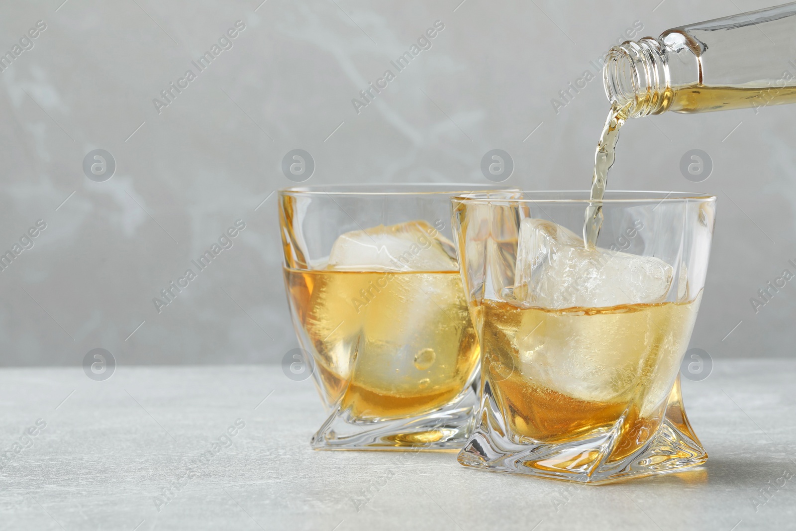 Photo of Pouring whiskey from bottle into glass at light table, closeup. Space for text