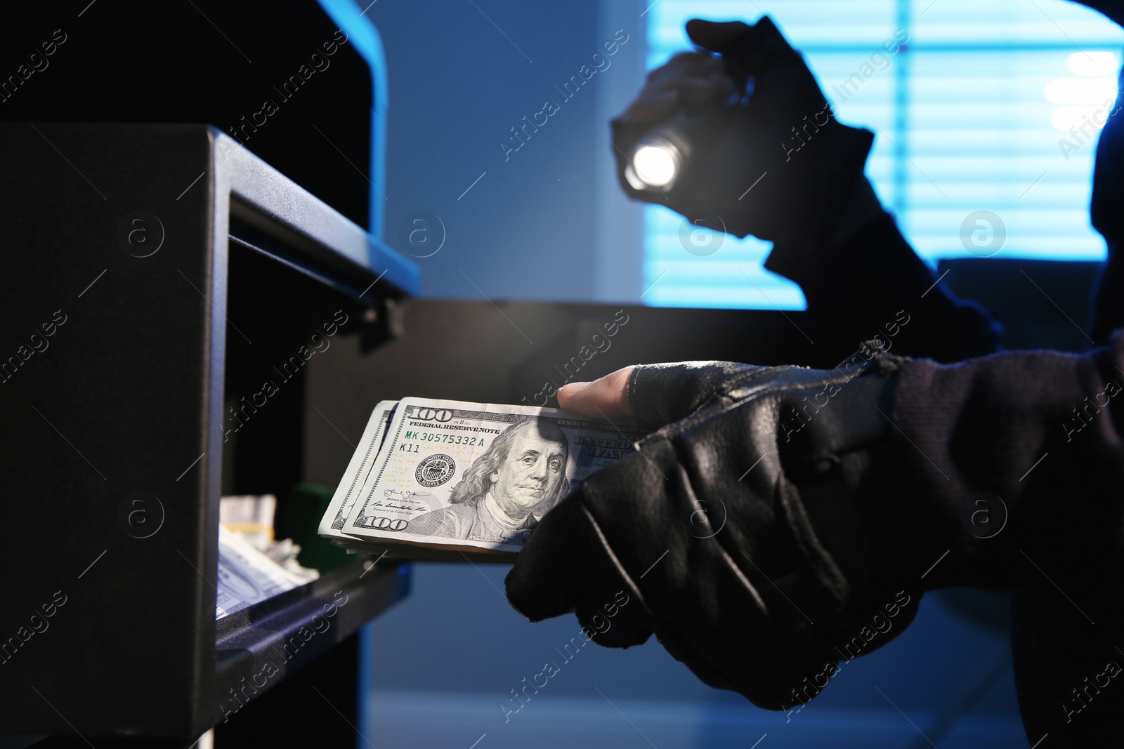 Photo of Thief taking money out of steel safe indoors at night, closeup