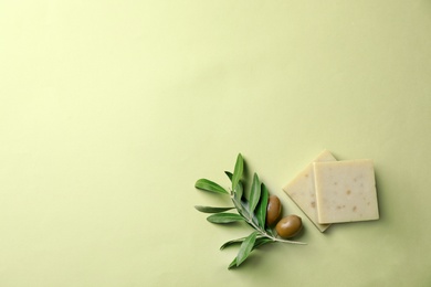 Handmade soap bars and leaves with olives on color background, top view with space for text