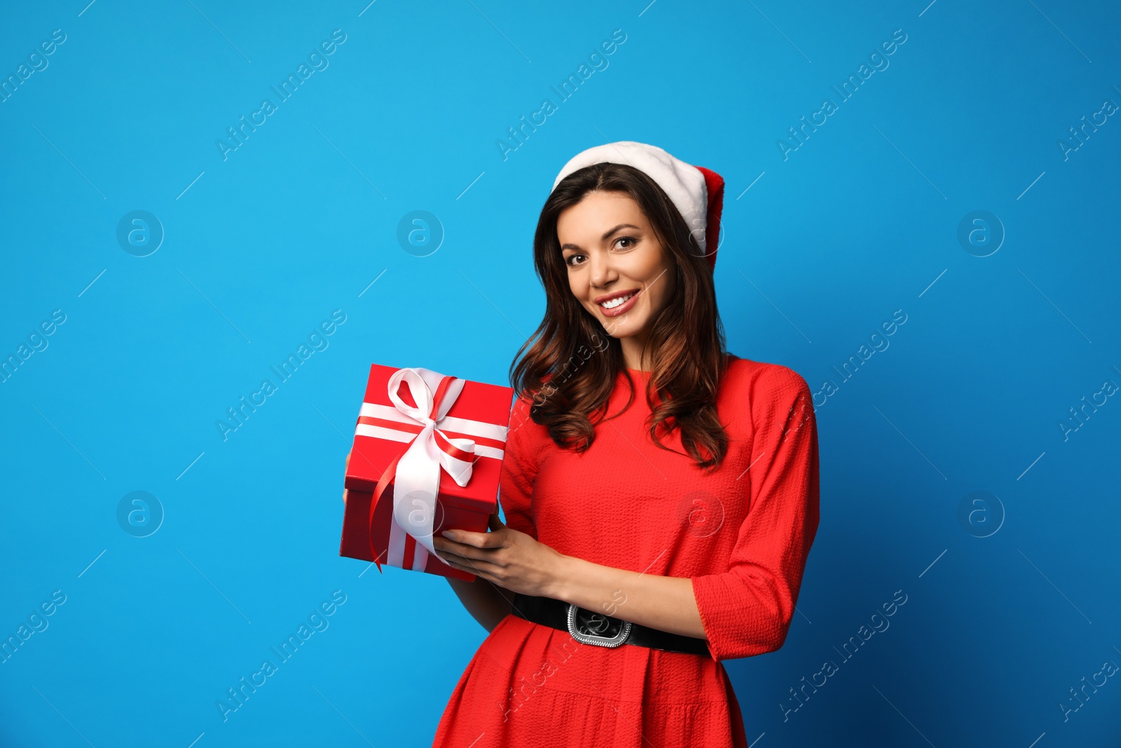 Photo of Beautiful woman wearing Santa hat with Christmas gift on light blue background