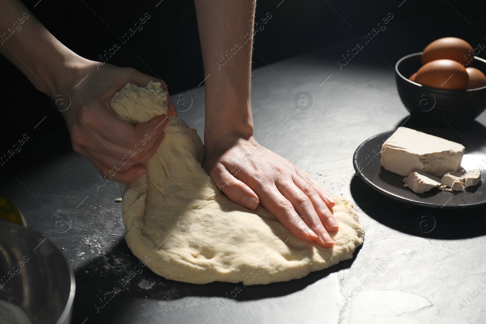 Photo of Making bread. Woman kneading dough at black table on dark background, closeup