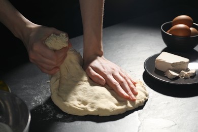 Making bread. Woman kneading dough at black table on dark background, closeup