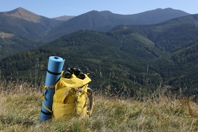 Backpack, sleeping pad and binoculars in mountains on sunny day, space for text