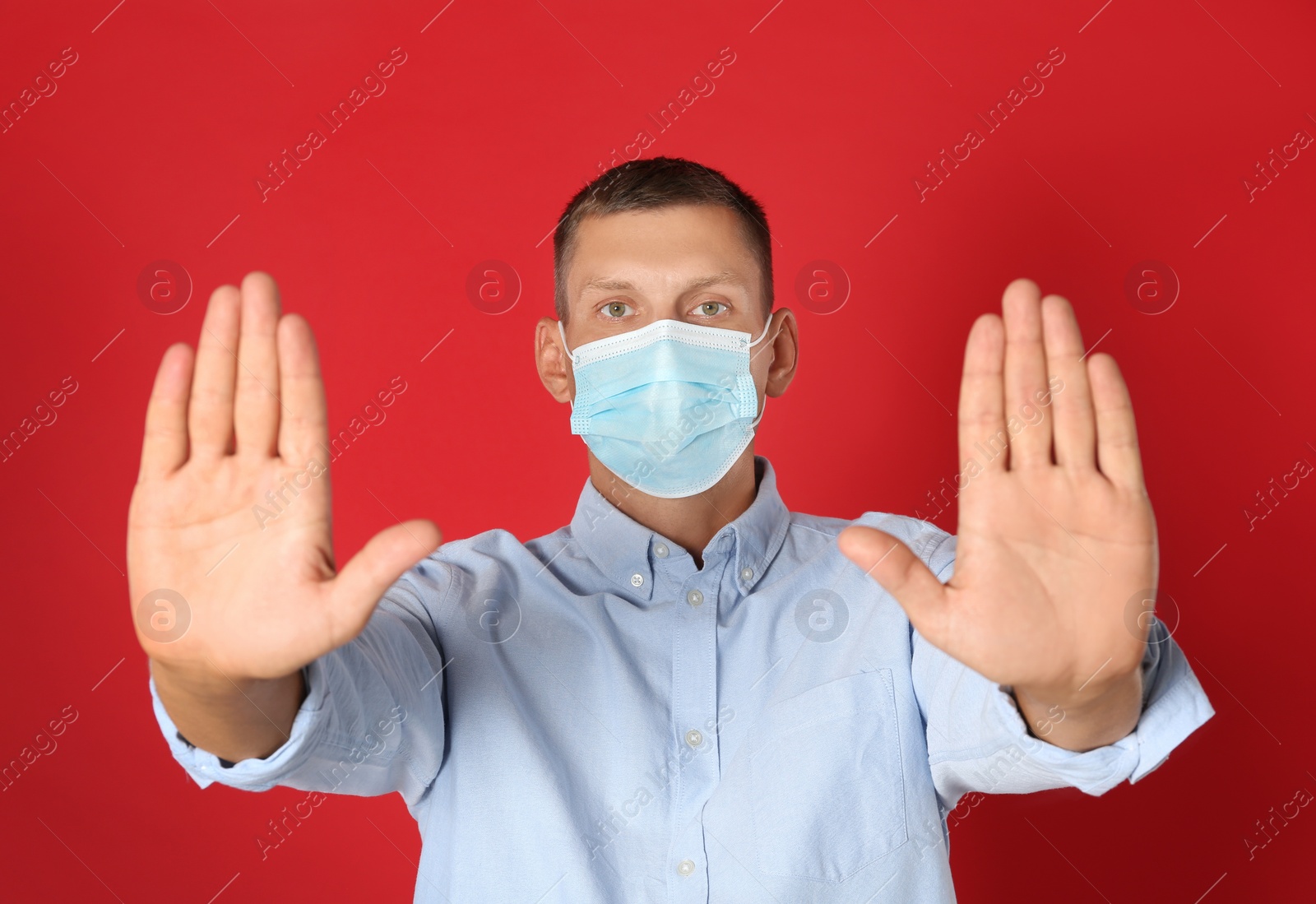 Photo of Man in protective mask showing stop gesture on red background. Prevent spreading of coronavirus