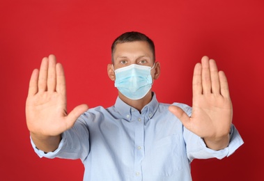 Photo of Man in protective mask showing stop gesture on red background. Prevent spreading of coronavirus