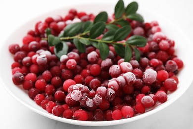 Photo of Frozen red cranberries and green leaves on white table, closeup