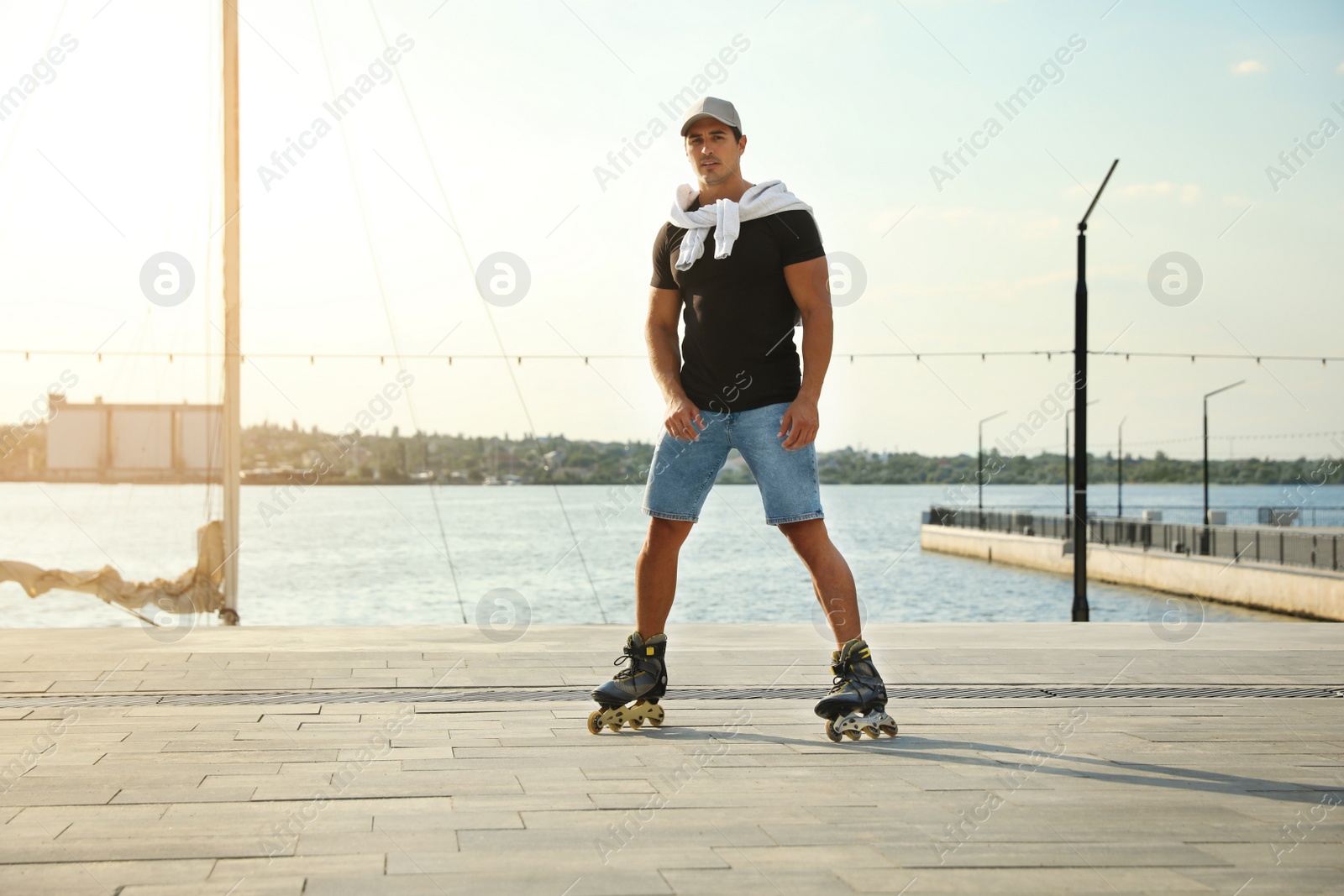 Photo of Handsome young man roller skating on pier near river, space for text