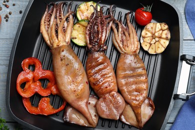 Photo of Tasty grilled squids with vegetables served on grey wooden table, flat lay
