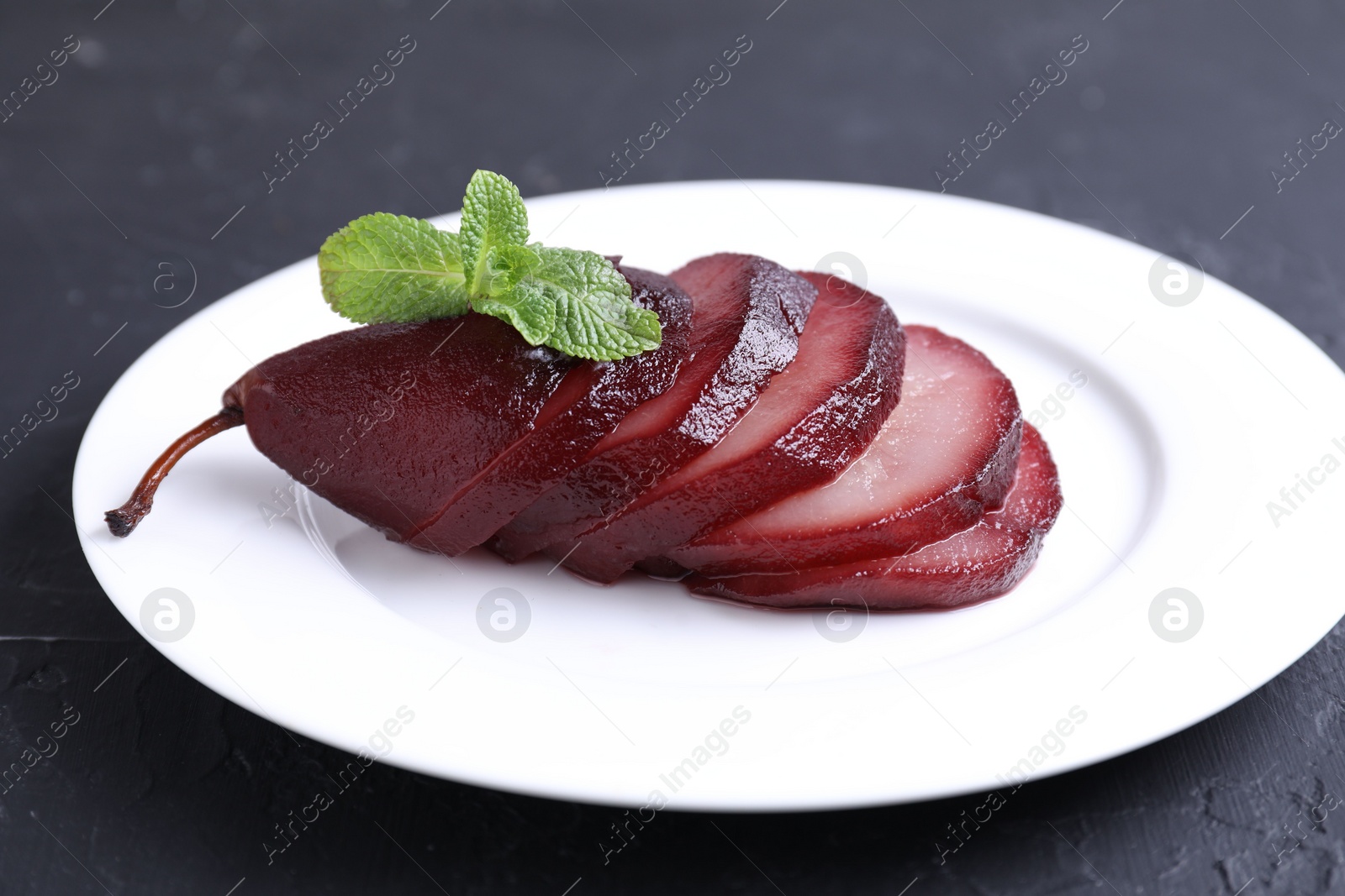 Photo of Tasty red wine poached pear and mint on black table, closeup