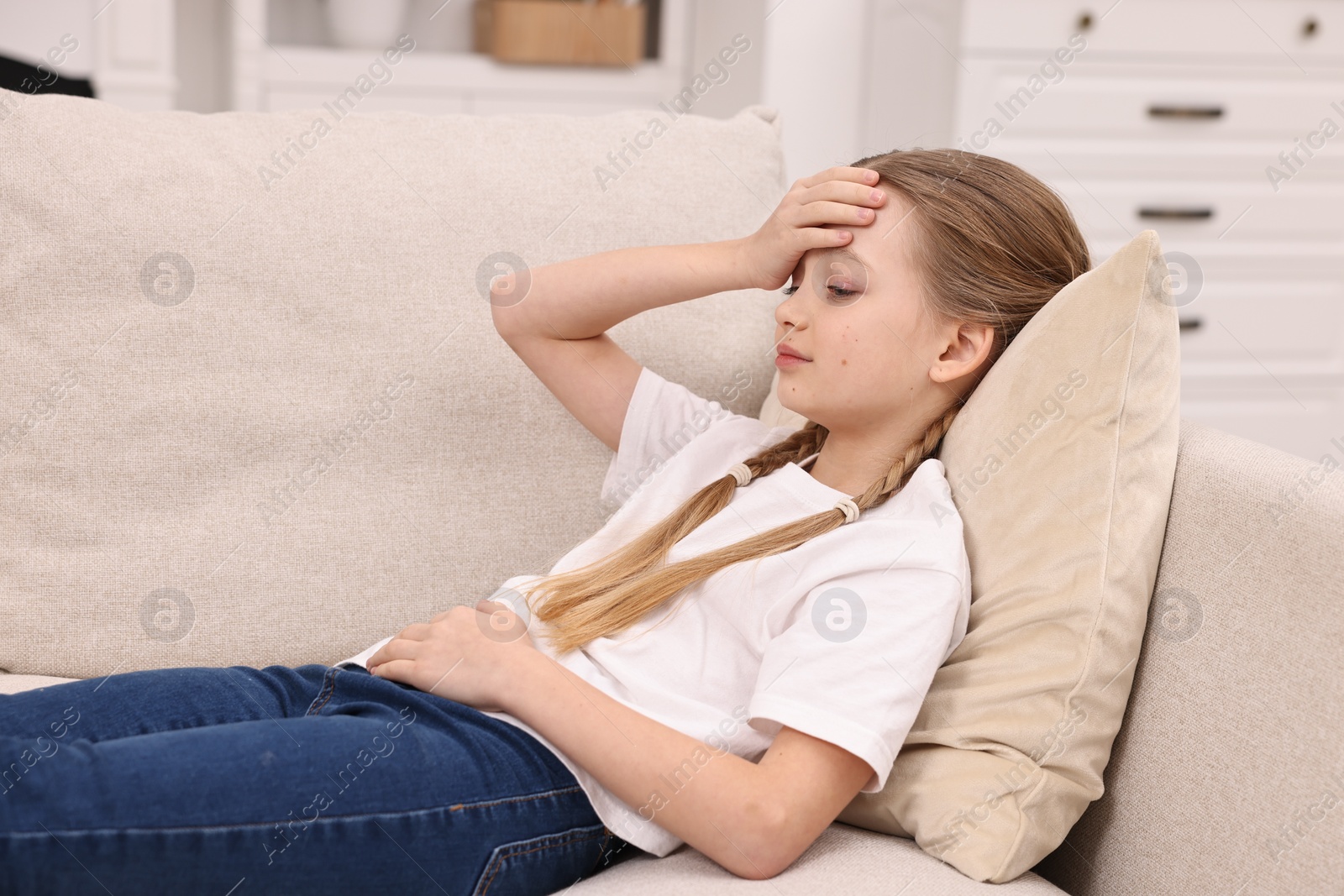 Photo of Little girl suffering from headache on sofa indoors