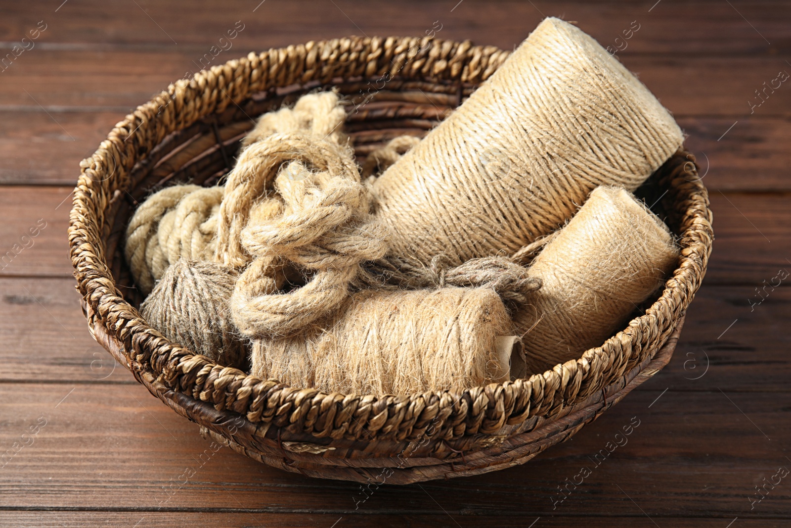 Photo of Natural hemp ropes in wicker basket on wooden table