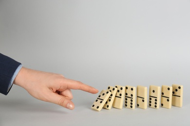 Photo of Woman causing chain reaction by pushing domino tile on grey background, closeup. Space for text
