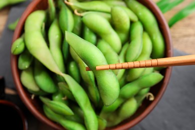 Photo of Taking edamame beans in pod from bowl with chopsticks, closeup